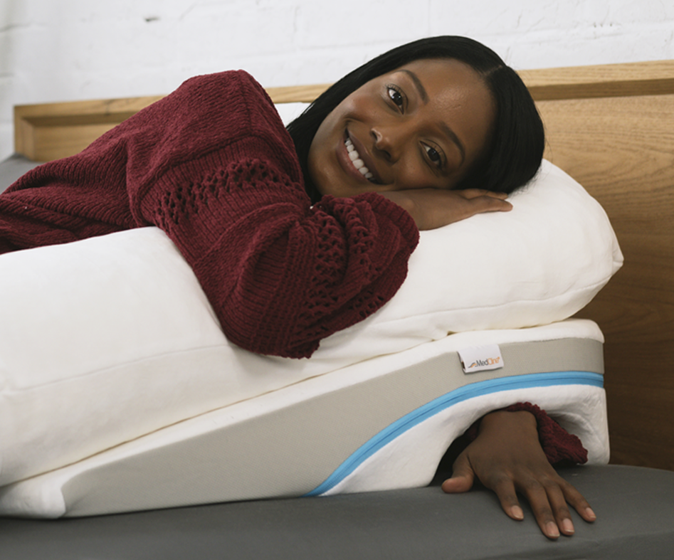 Smiling woman lying on a therapeutic body pillow and wedge, resting her arm in the built-in pocket.