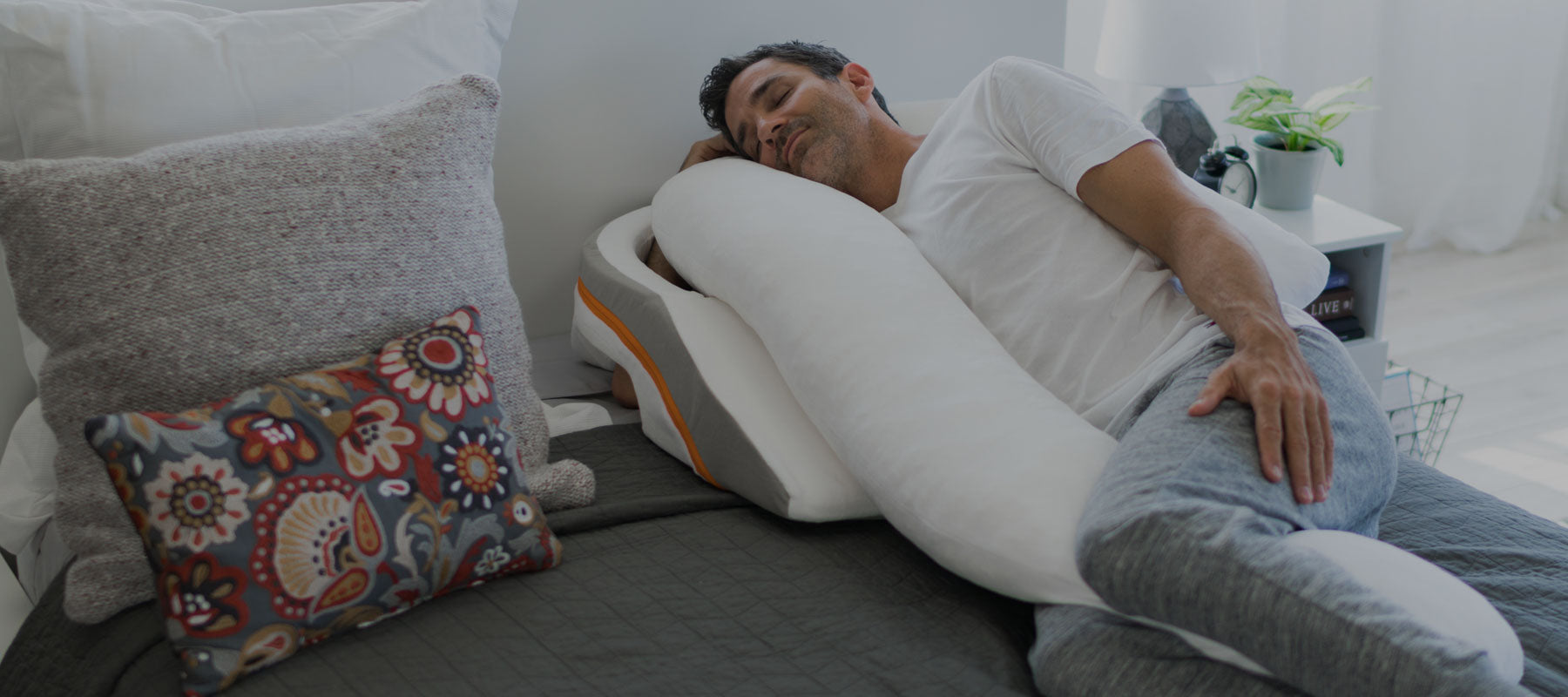 Man sleeping comfortably on a therapeutic body pillow with an incline wedge in a cozy bedroom.