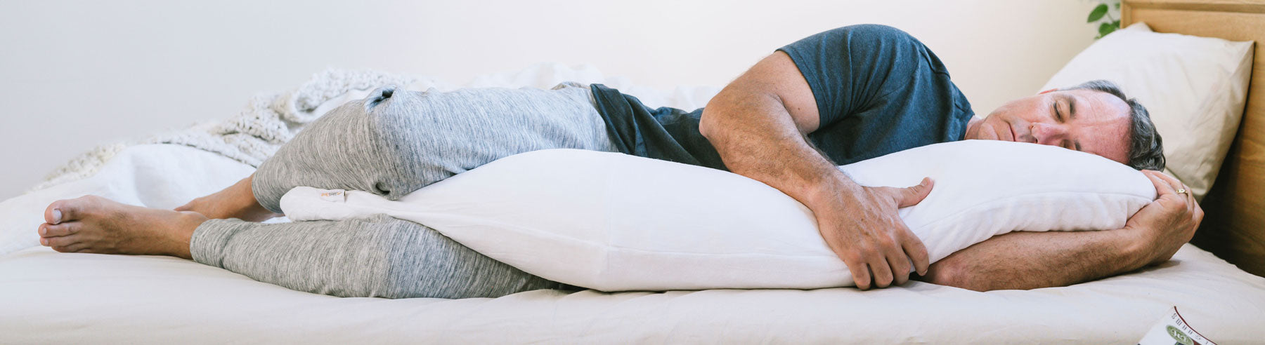 Man comfortably sleeping on his side, hugging a full-body pillow with his arms and legs.